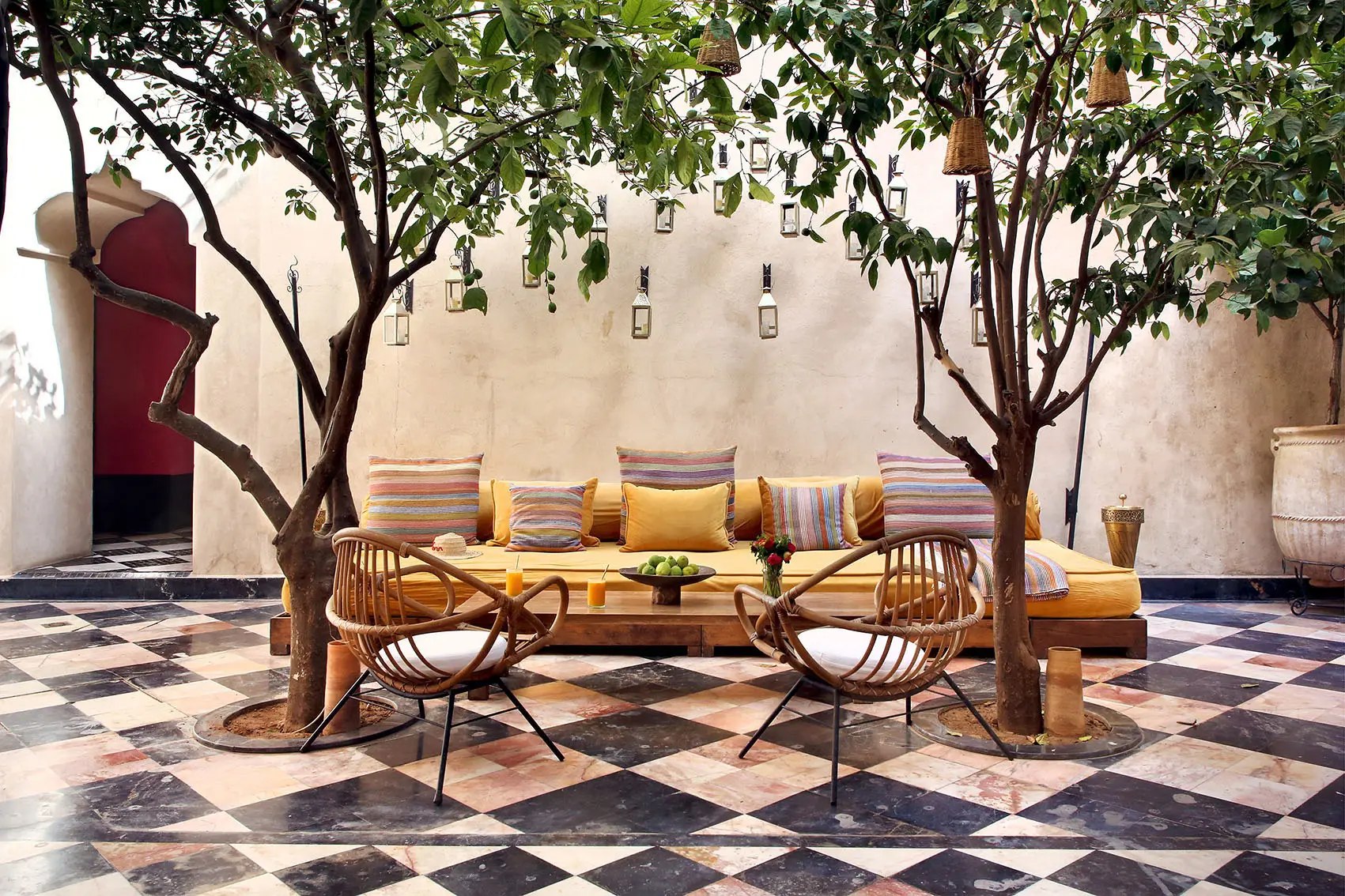Patio à sol en damier, arbres et banquette jaune. El Fenn, Marrakech.