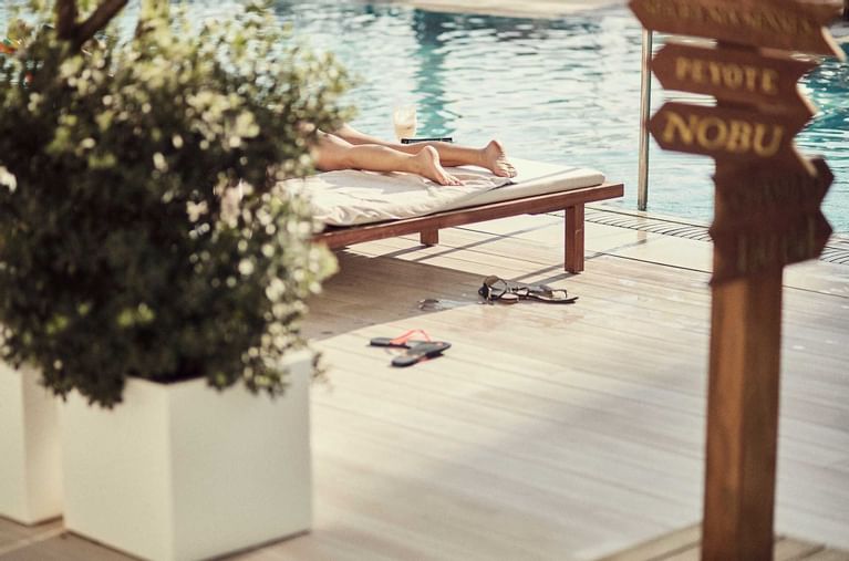 Lit de repos en bois, plante et panneau Nobu dans les espaces extérieurs du Nobu Hotel Ibiza Bay.
