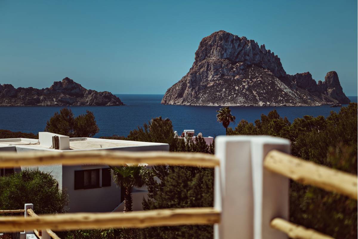 Vue sur Es Vedrà et la mer depuis une terrasse du Petunia, au-dessus des bâtiments blancs.