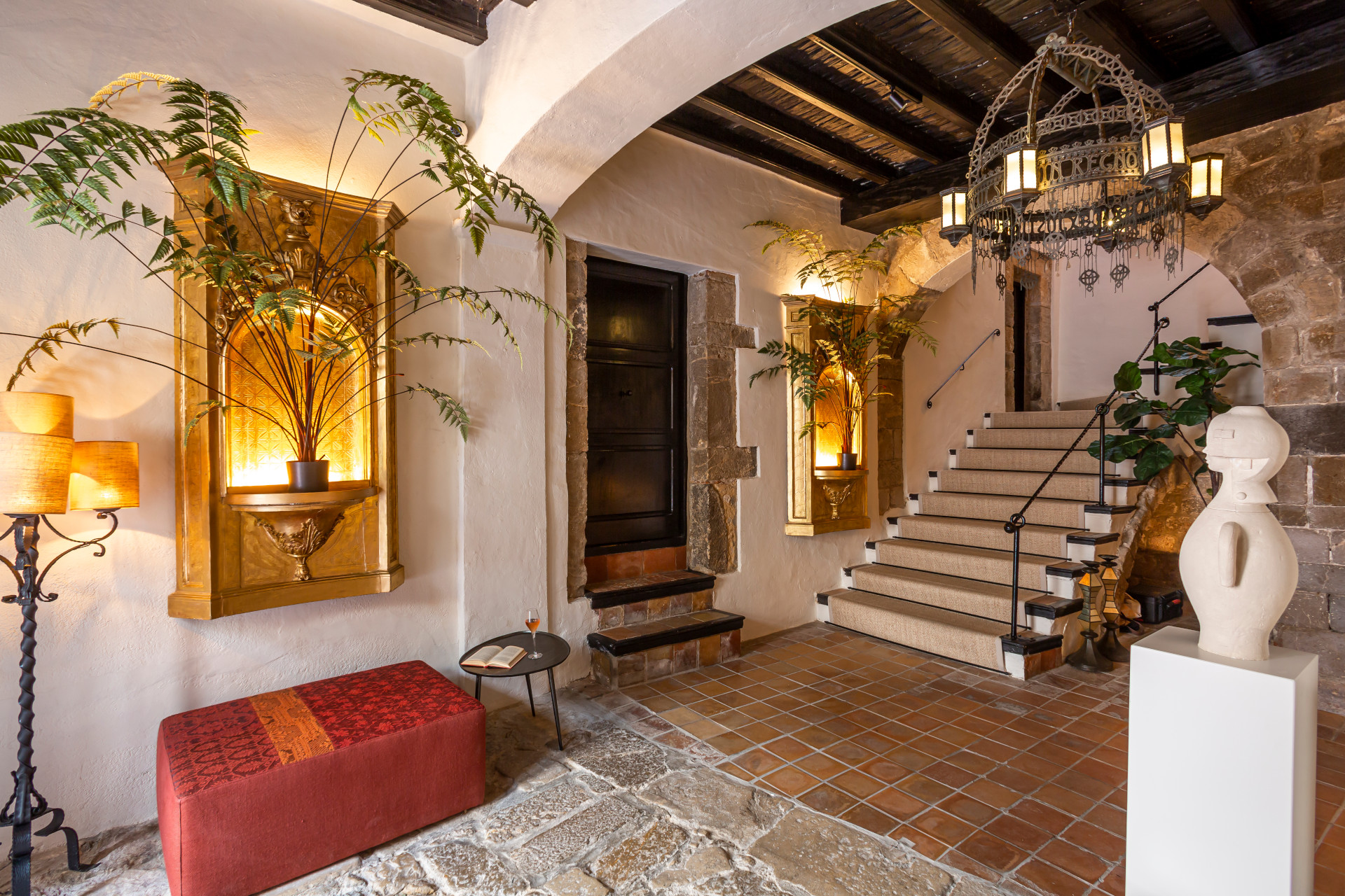 Hall de La Torre del Canónigo, escalier de pierre, poutres, plantes et banquette rouge.