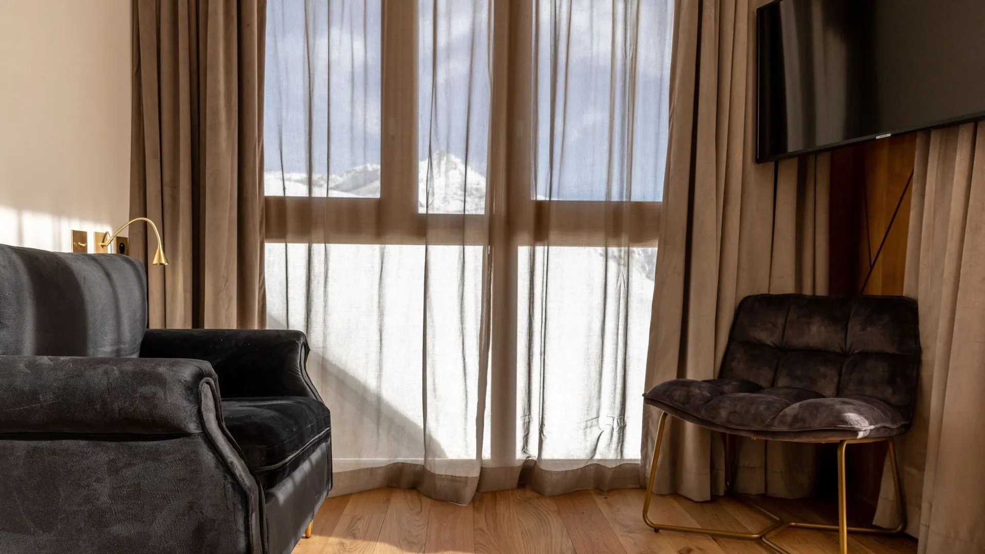 Salon d’une suite du Diamond Rock à Tignes, avec canapé, fauteuil et grandes fenêtres sur la montagne enneigée.