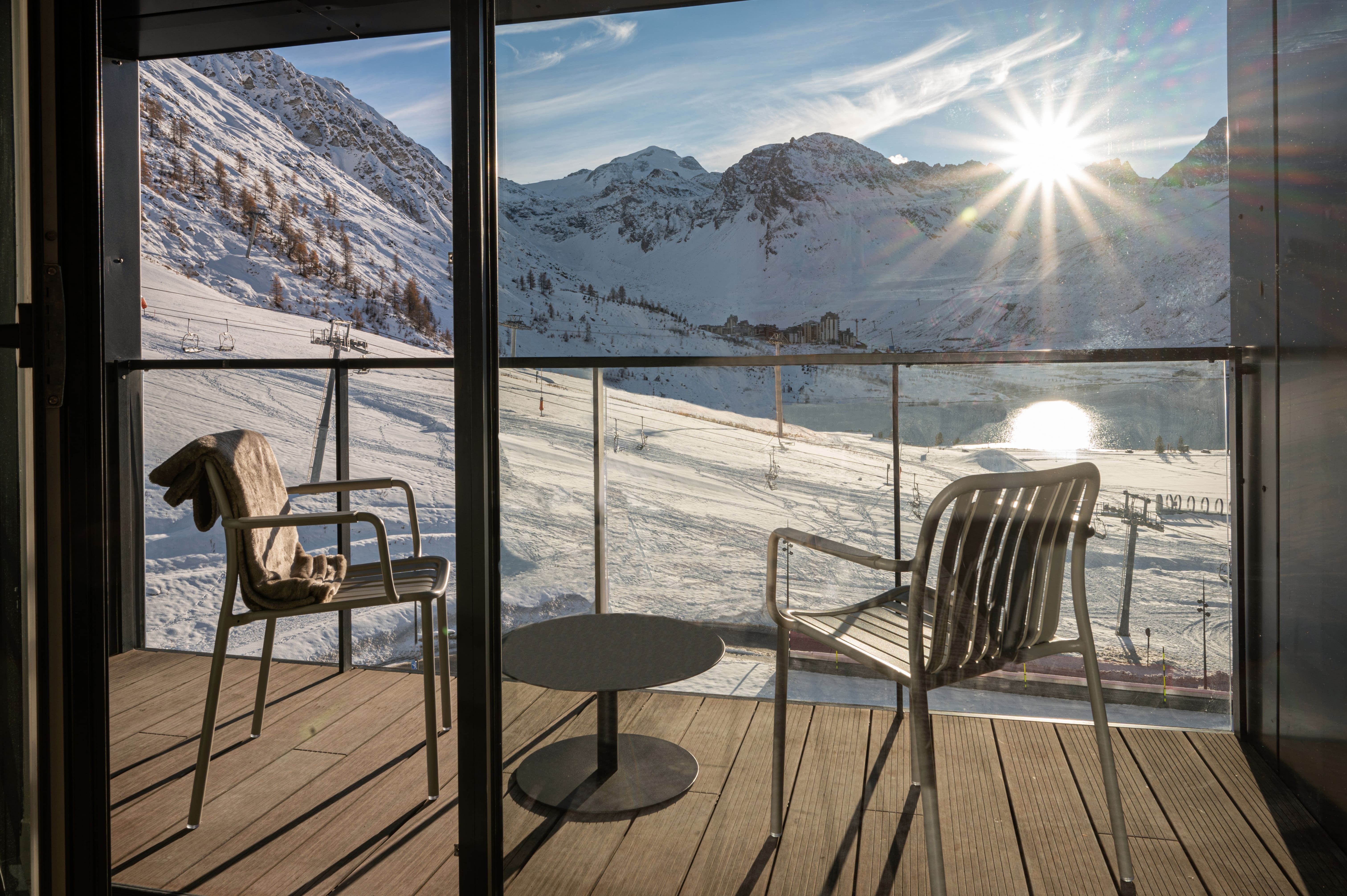 Terrasse d’une chambre du VoulezVous à Tignes, avec deux fauteuils devant les pistes et les sommets enneigés.