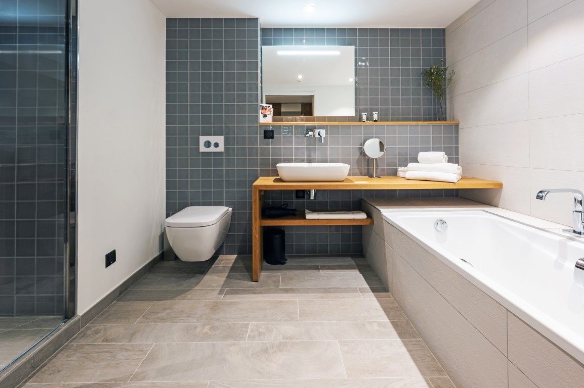 Salle de bains d’un hébergement communicant du VoulezVous à Tignes, avec baignoire, douche vitrée et carrelage bleu gris.