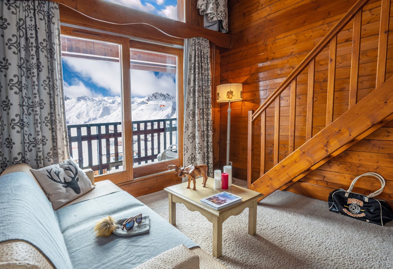 Salon de la Suite Junior Mezzanine des Campanules à Tignes, avec escalier de bois et baie sur les montagnes.