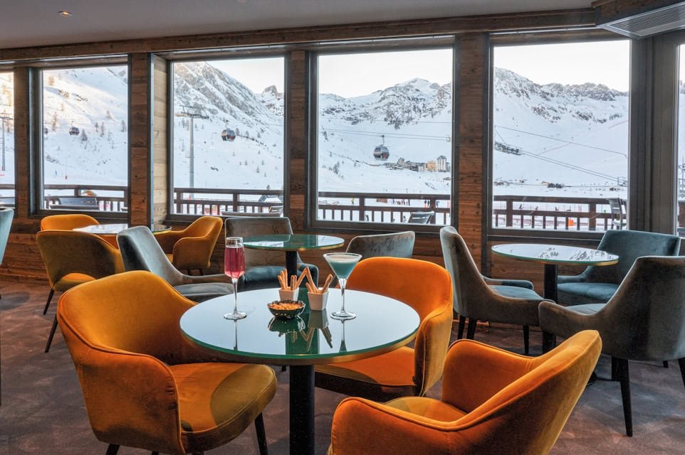 Fauteuils orange et gris du bar Le Pompon au Levanna, devant les baies vitrées sur les pistes.