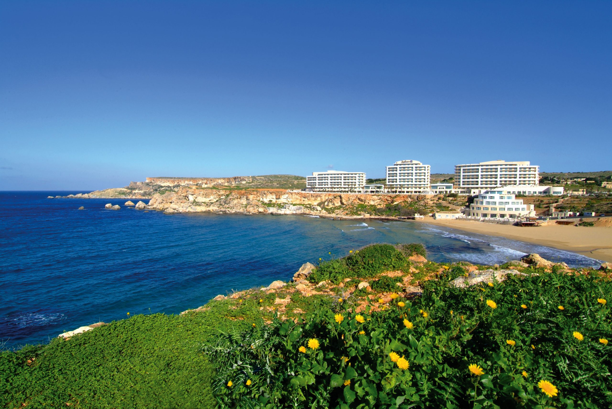 Le Radisson Blu Golden Sands à Malte, au-dessus de la baie, vu depuis un premier plan fleuri.