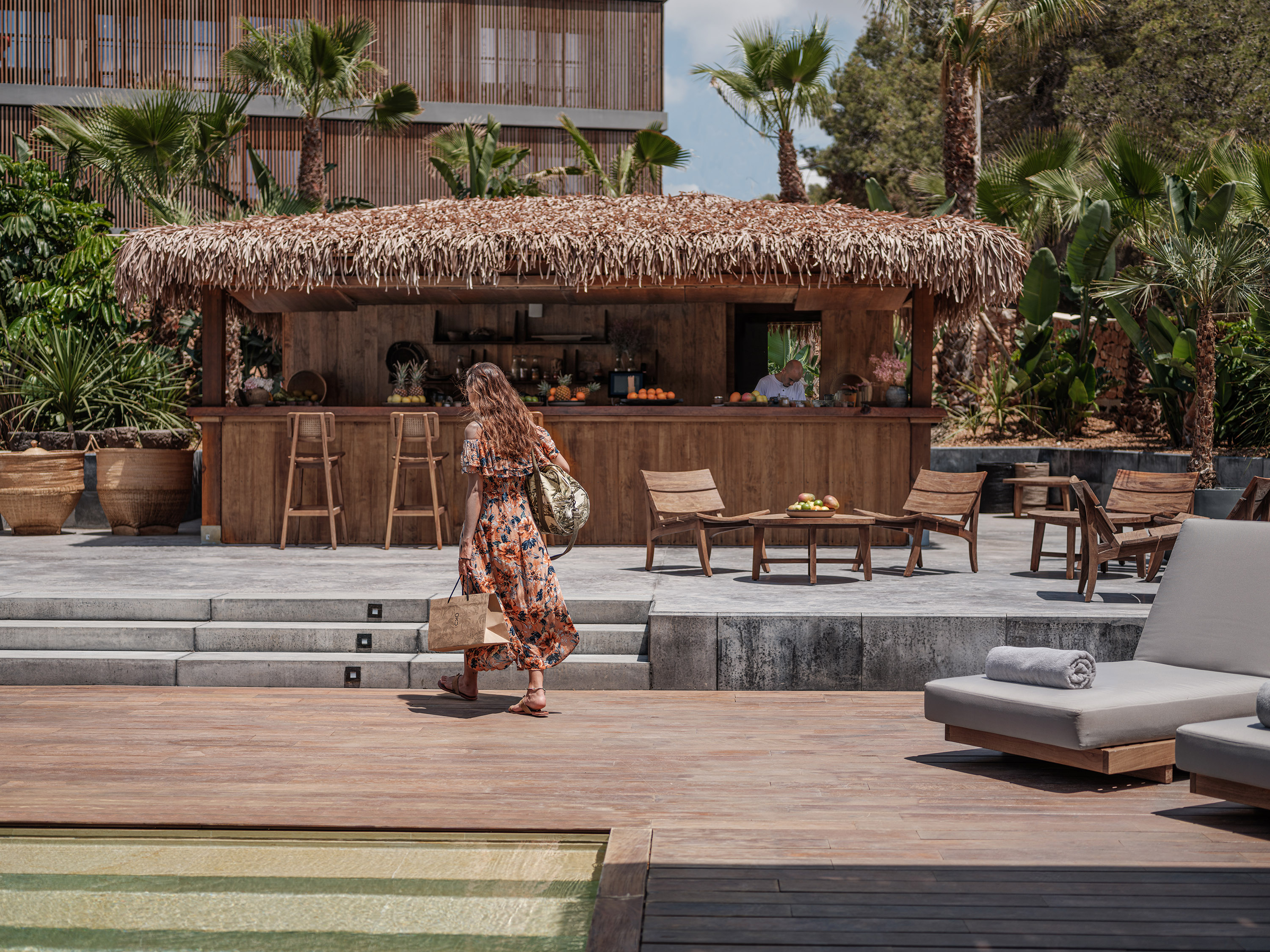 Juice bar d'OKU Ibiza sous un toit de chaume, devant les palmiers et les bâtiments de l'hôtel.