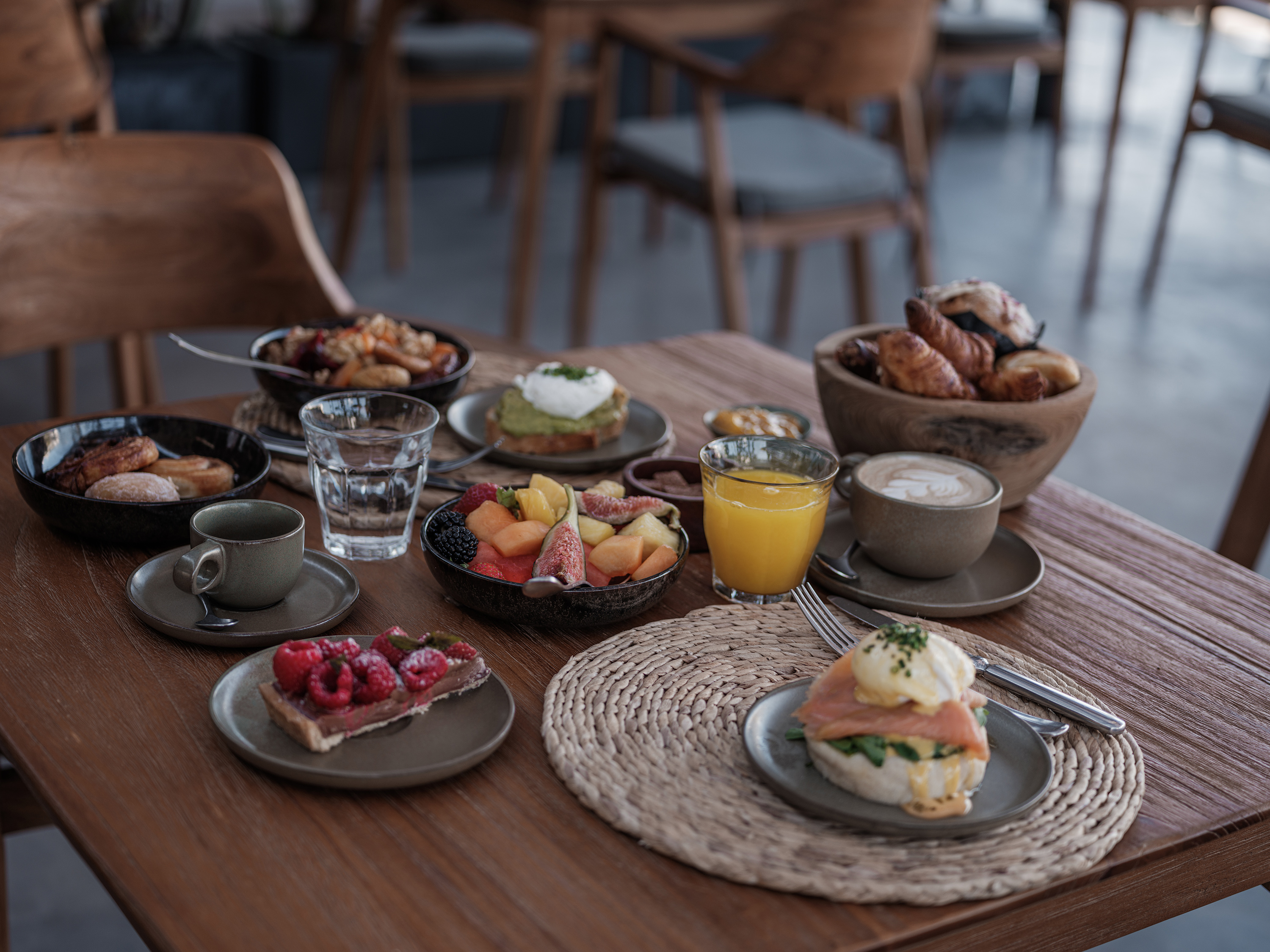 Petit déjeuner d'OKU Ibiza, avec fruits, viennoiseries, jus et assiettes servis sur une table en bois.