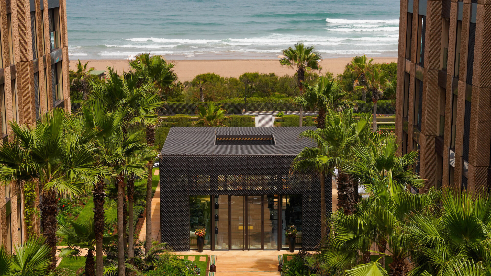 Jardins du Four Seasons Hotel Casablanca vus entre les deux ailes, avec pavillon et océan à l'arrière-plan.