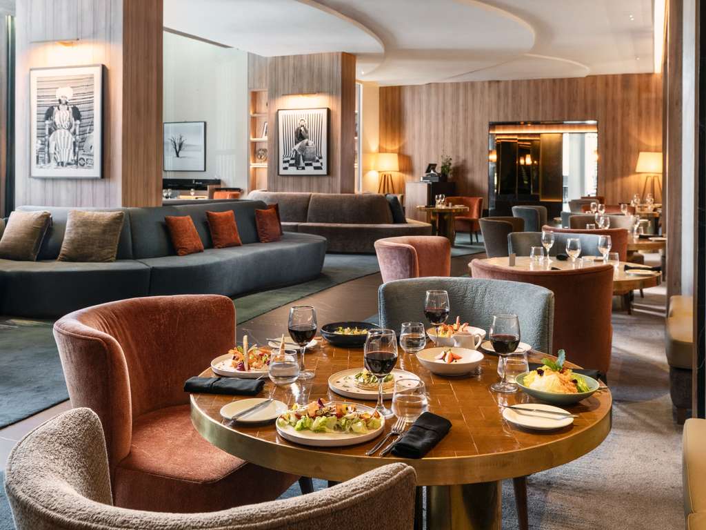 Table avec assiettes et verres à la Brasserie Flâneur du Sofitel Casablanca Tour Blanche, devant des canapés et portraits.
