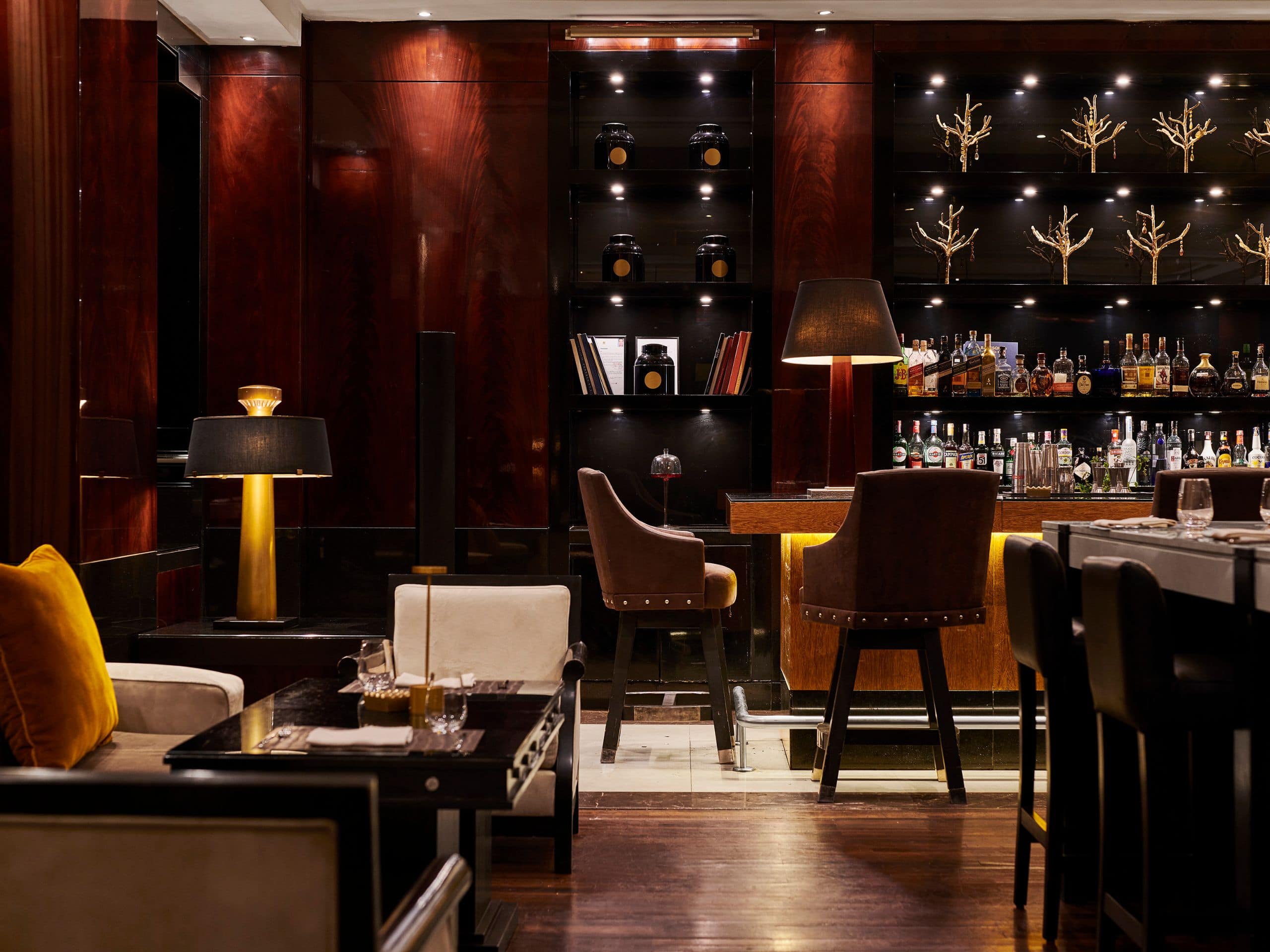 Comptoir du Living Room au Hyatt Regency Casablanca, avec tabourets et bouteilles éclairées dans les boiseries sombres.