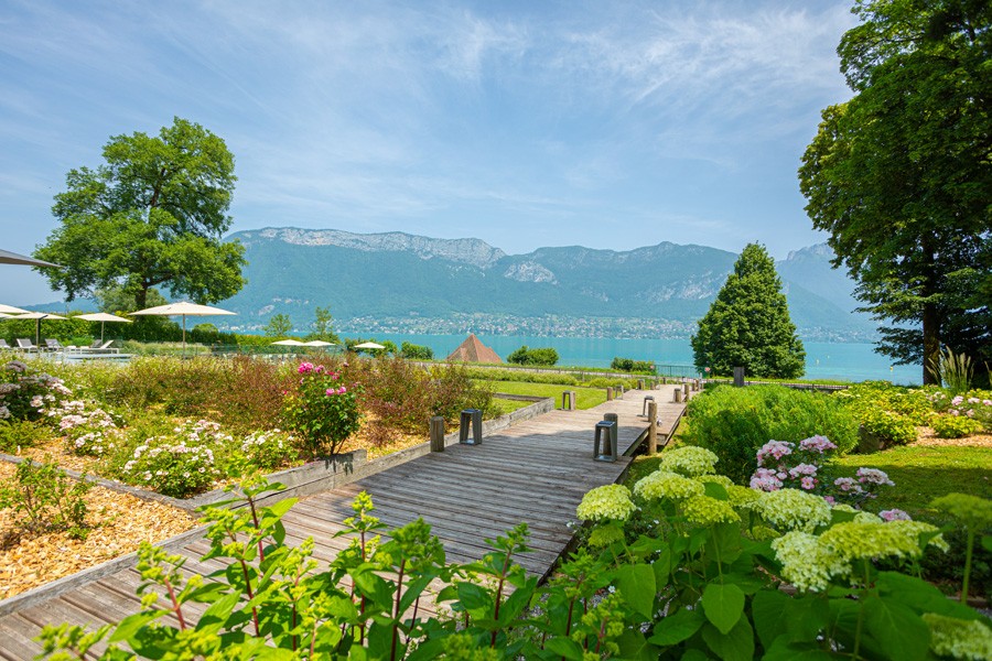 Passerelle en bois du jardin du Black Bass Hotel à Sévrier, entre hortensias et lac.