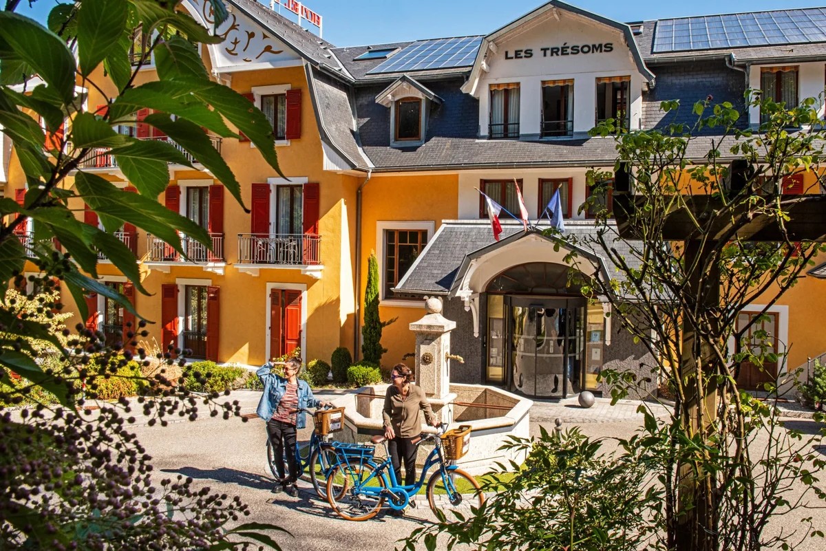 Entrée de l'hôtel Les Trésoms à Annecy, façade jaune à volets rouges et vélos au premier plan.