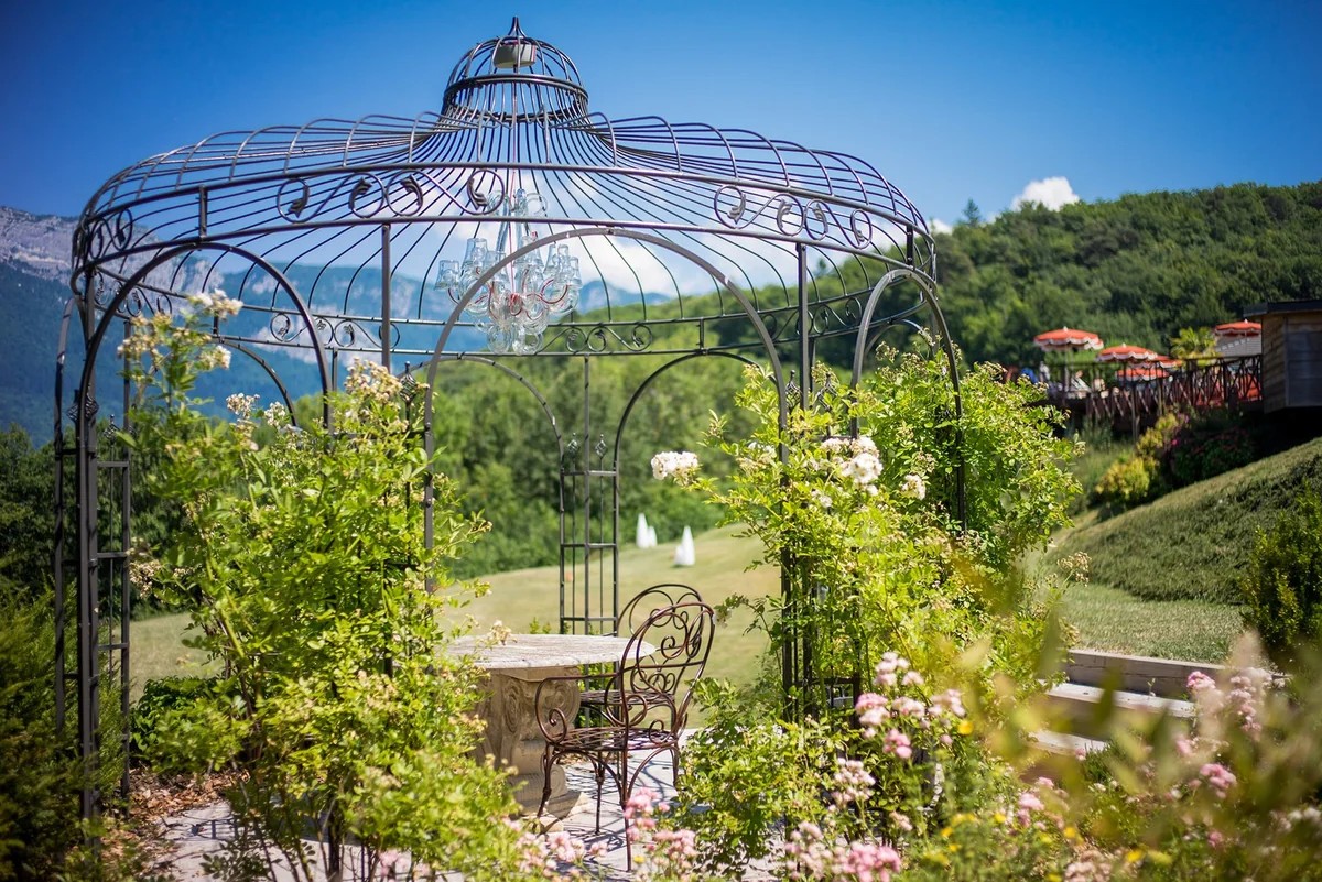 Gloriette métallique et salon de jardin des Trésoms, entourés de fleurs au-dessus du lac d'Annecy.