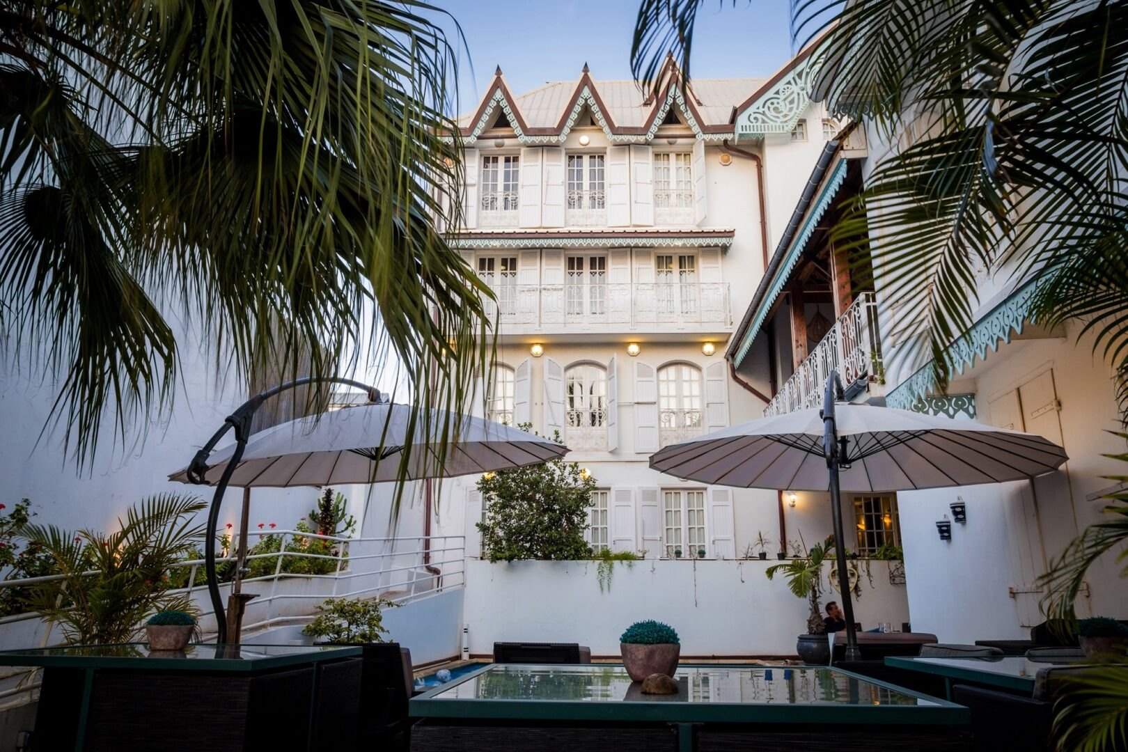 La façade créole blanche de l'Hôtel Le Juliette Dodu à Saint-Denis, balcons à lambrequins et patio aux parasols