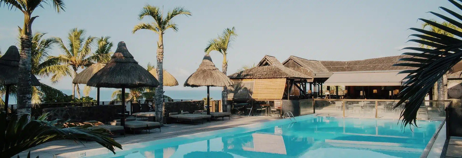 La piscine principale de l'Iloha Seaview Hotel, paillotes et palmiers devant l'océan Indien