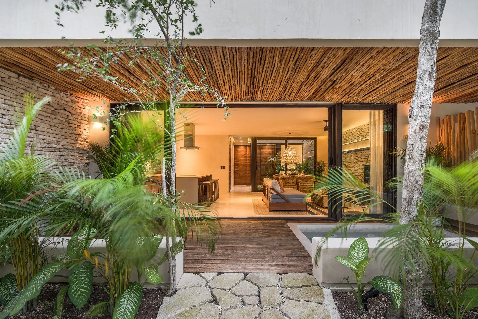 Une villa du Copal Tulum Hotel éclairée à la nuit tombante, sa piscine privée et son auvent de rondins