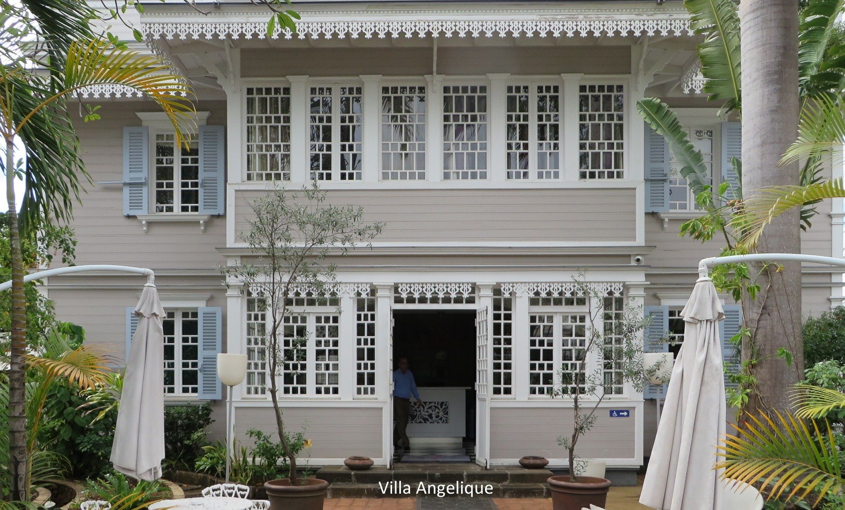 La façade de la Villa Angélique vue de face depuis le jardin, varangue à lambrequins ajourés et persiennes bleues