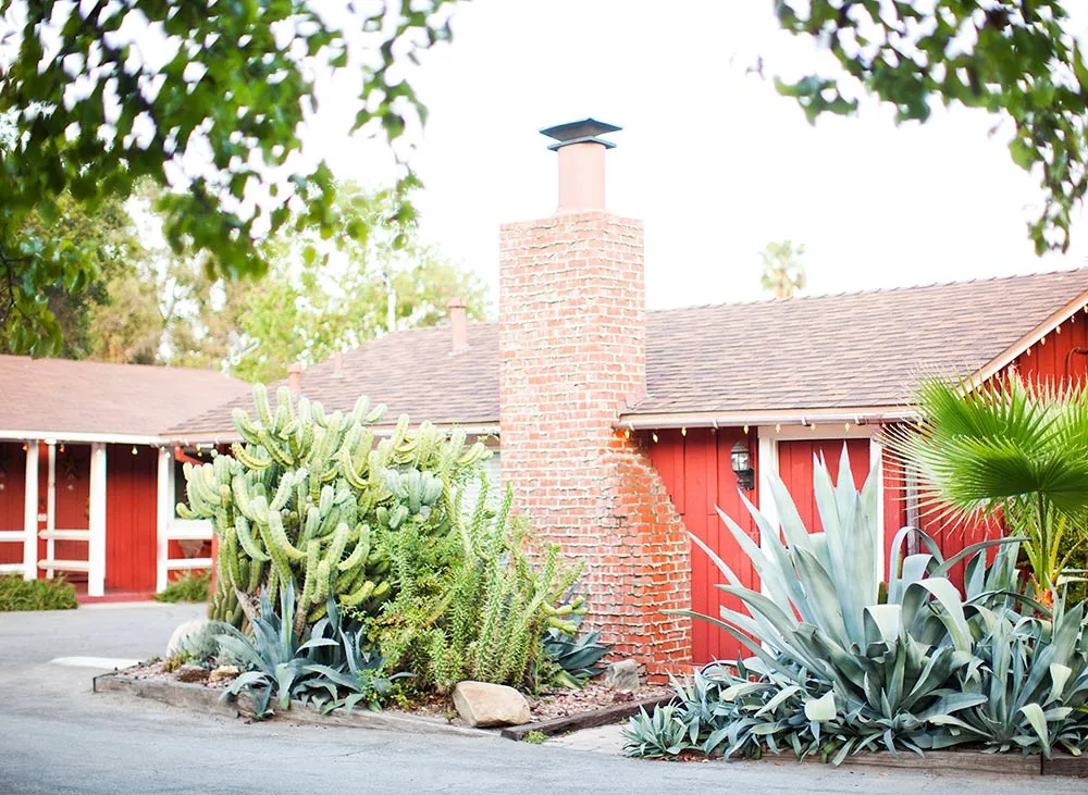 Façade rouge du motel, cheminée de brique et jardin d'agaves à l'entrée de la propriété