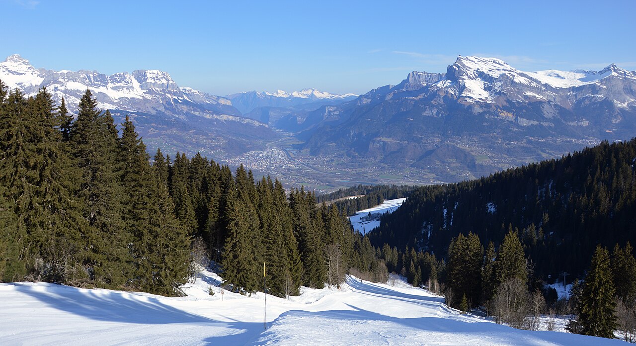 Piste bordée de sapins côté Demi-Quartier, avec Sallanches et la vallée de l'Arve au loin