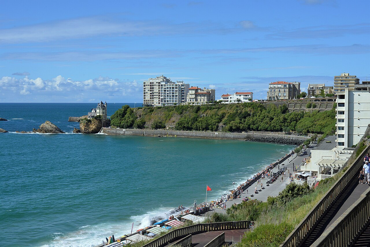 La plage de la Côte des Basques à Biarritz vue des escaliers de la falaise, mer haute et drapeau rouge, avec la villa Belza sur son rocher au fond