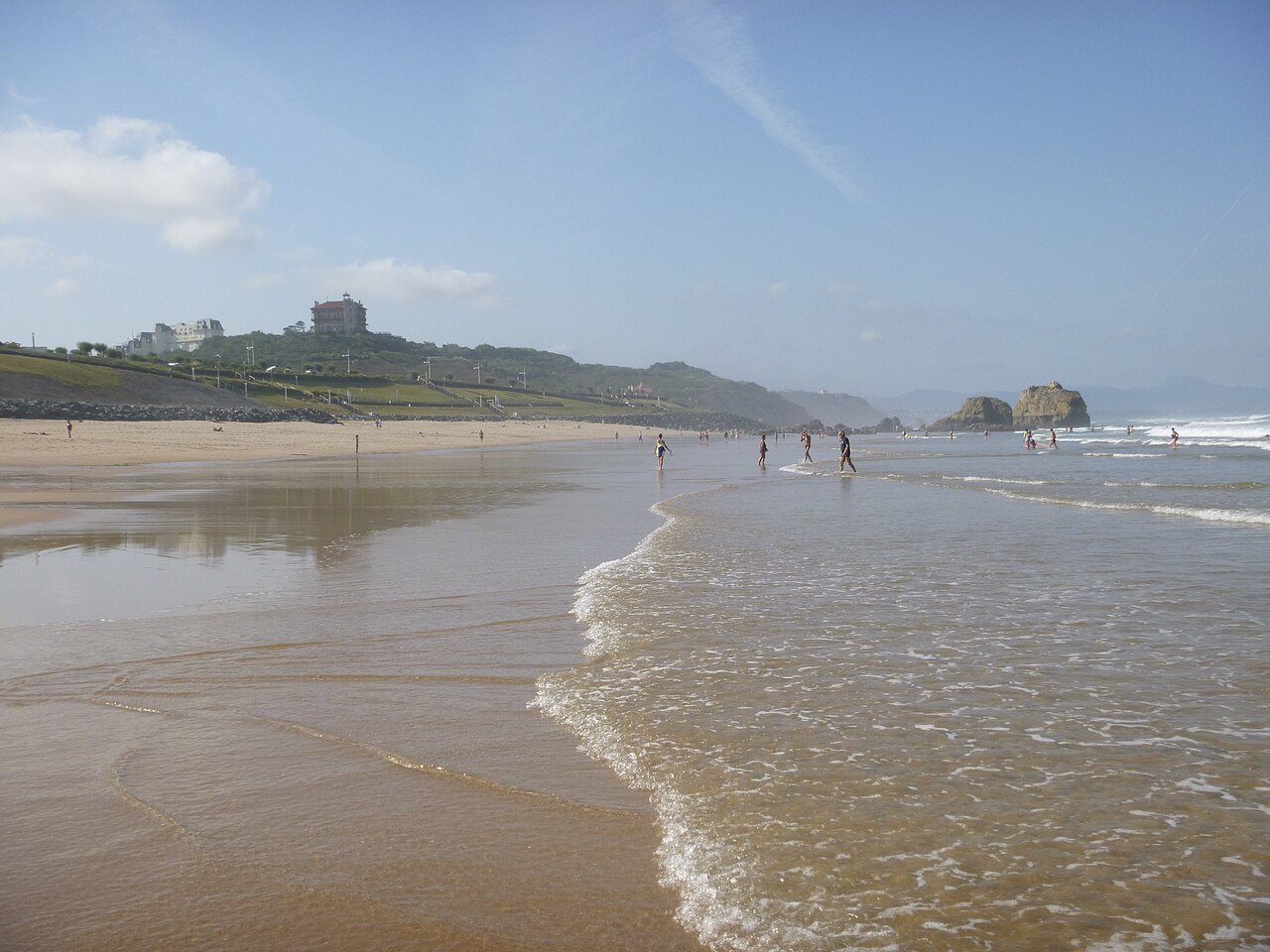 La plage de la Milady à Biarritz à marée basse, baigneurs dans les vagues et rochers de la côte sud au loin