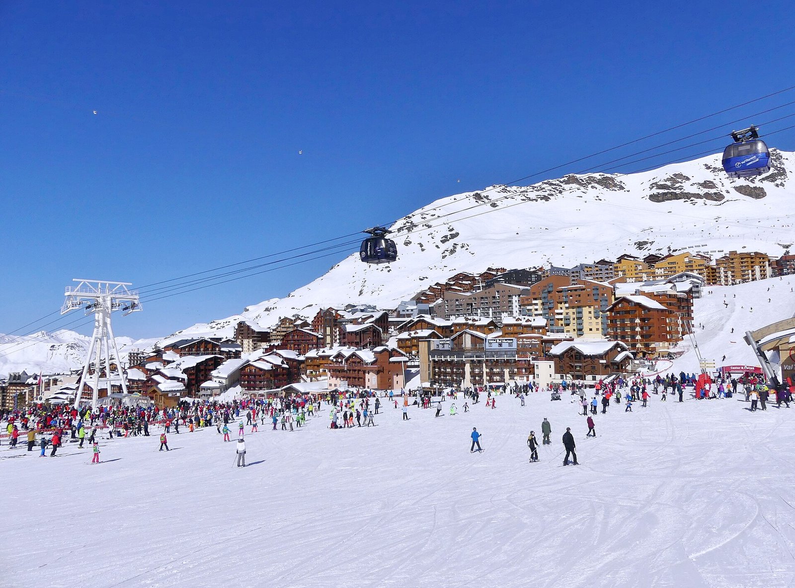 Le front de neige de Val Thorens, où se rejoignent les principales pistes, en février 2019 : skieurs au pied des immeubles du bas de la station, sous les cabines d'une télécabine.