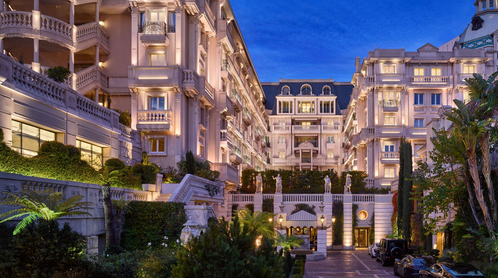Façade Belle Époque illuminée et jardin d'entrée de l'Hôtel Métropole Monte-Carlo à la tombée de la nuit, Monaco