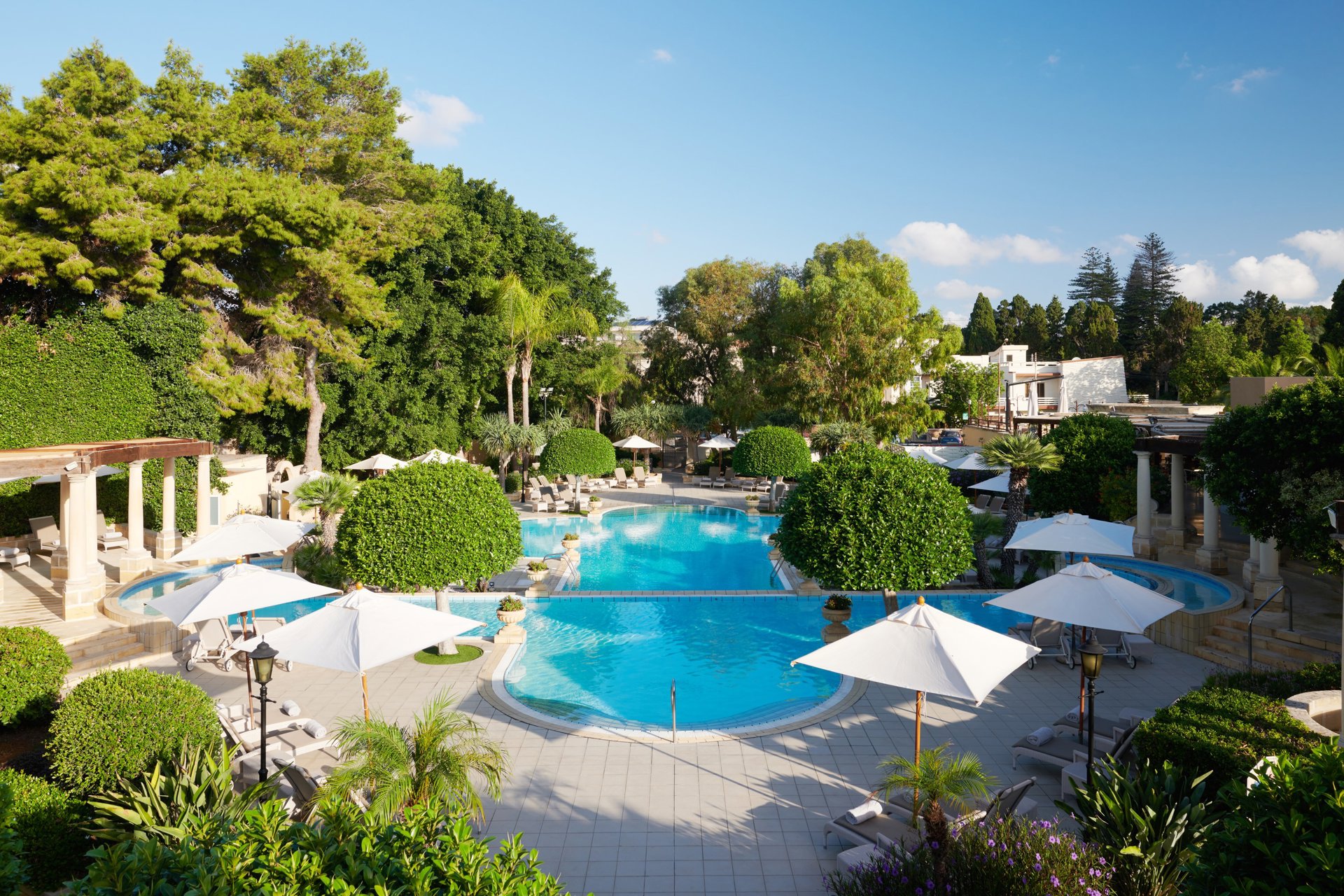 Piscine extérieure entourée de jardins et parasols au Corinthia Palace Malta, à San Anton sur l'île de Malte.