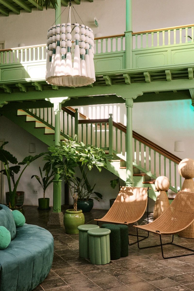 Salon vert du César Lanzarote avec escalier, fauteuils et plantes sous la verrière.