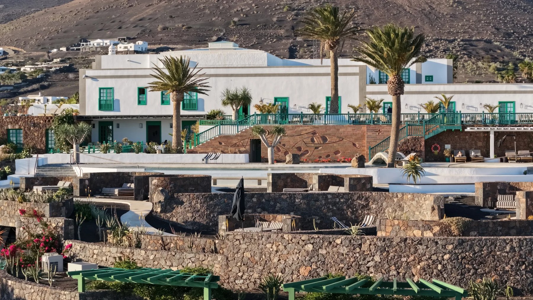 Façade blanche du César Lanzarote entourée de pierres sombres et de plantations.
