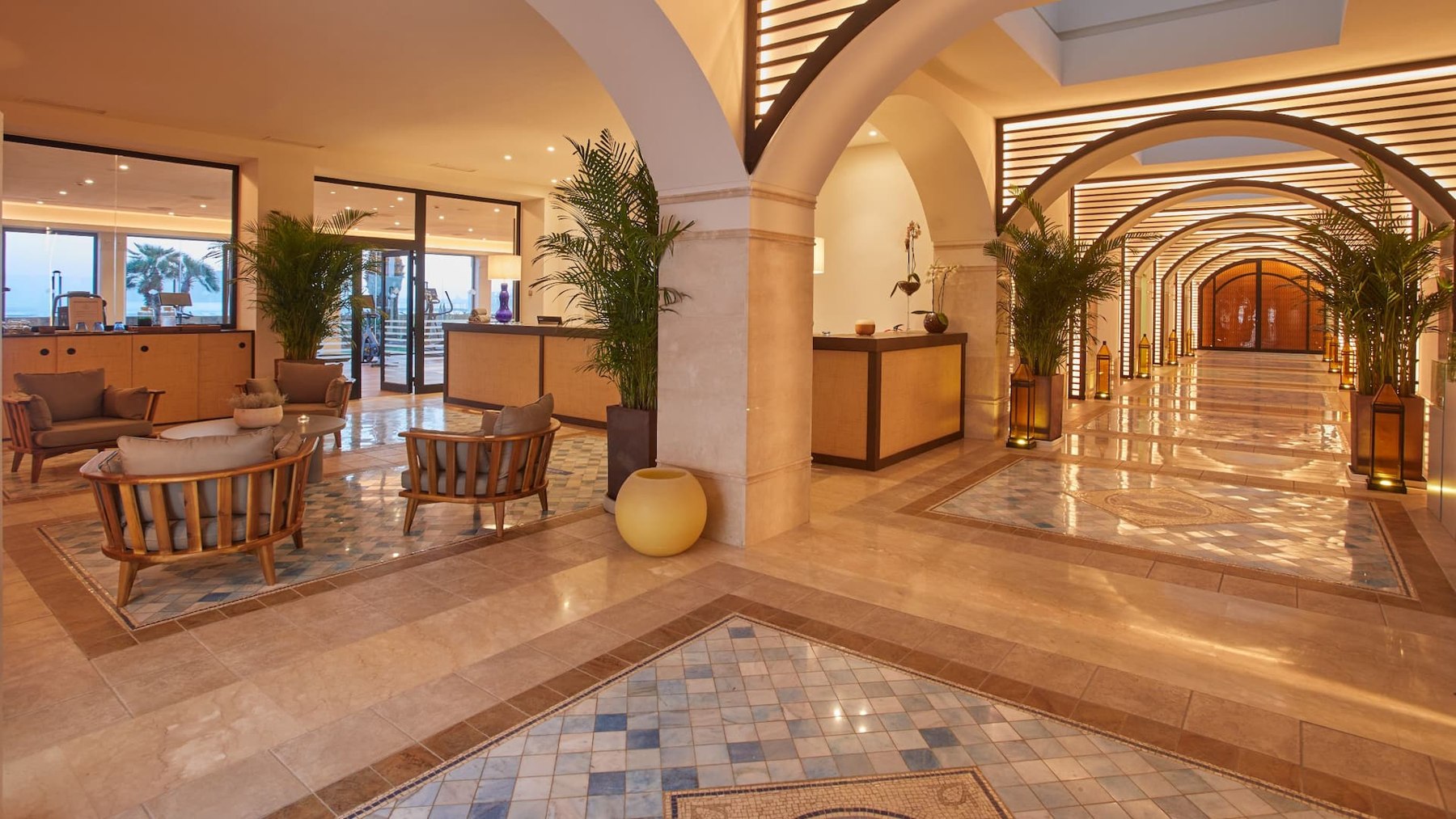 Galerie intérieure du Secrets Bahía Real avec arcades, plantes et assises claires.