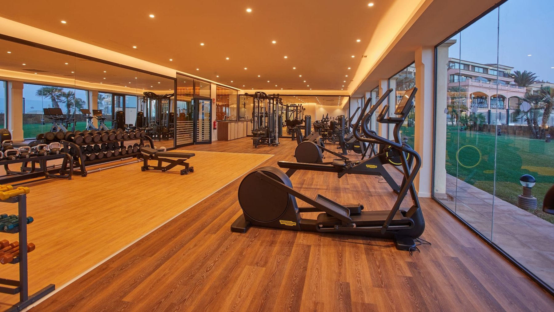 Salle de fitness du Secrets Bahía Real avec machines et larges baies vitrées.