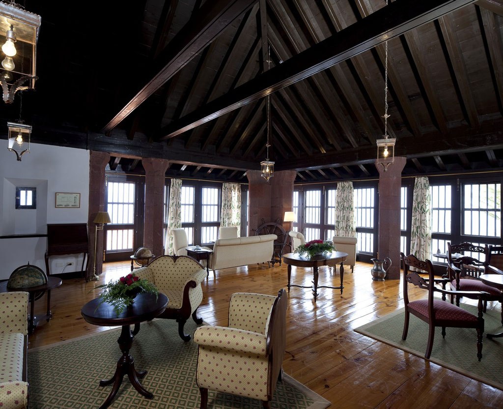 Grand salon du Parador de La Gomera sous une charpente sombre, avec fauteuils et baies vitrées.