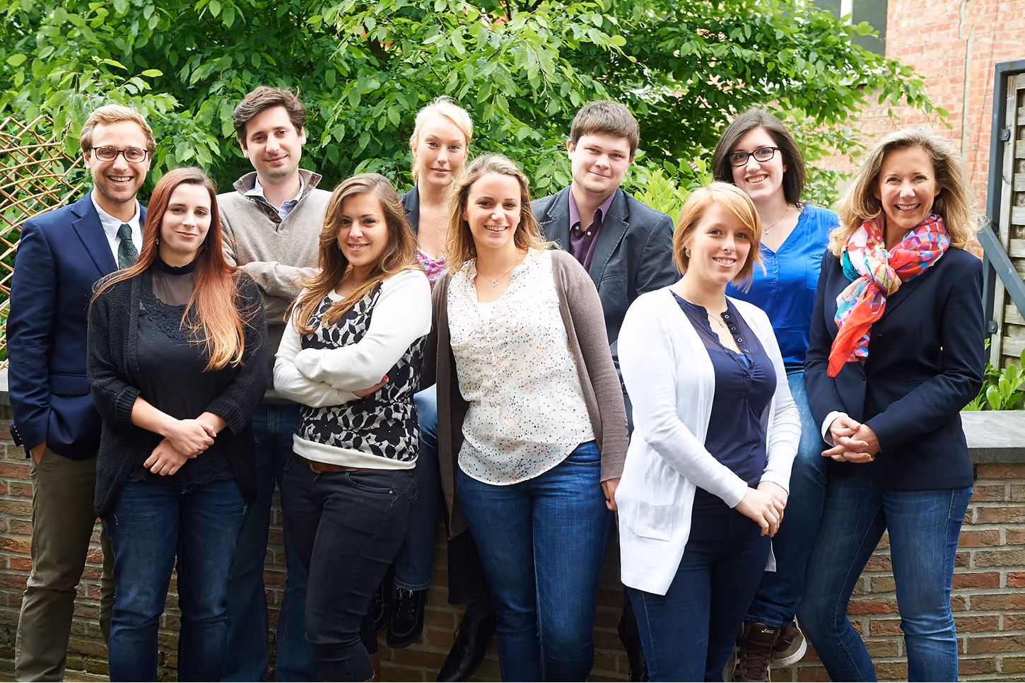 blue2purple - Team posing outdoors in front of greenery and a brick wall
