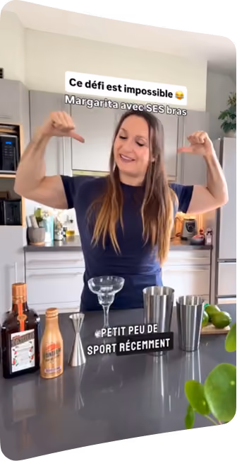 blue2purple - A woman flexing her arms behind a kitchen counter set with cocktail shakers and a glass
