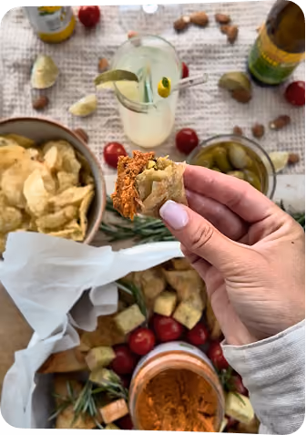blue2purple - A hand holding a cracker with red dip above a grazing board of crisps, tomatoes and pickles