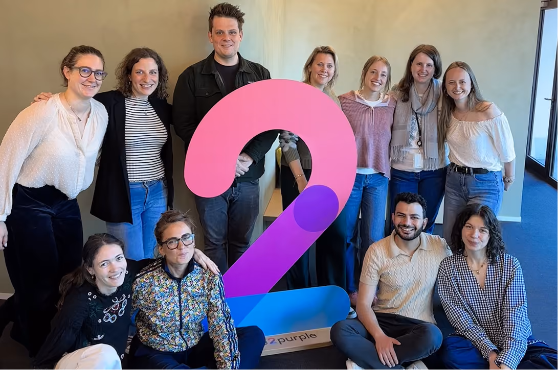 blue2purple - Team posing around the pink and purple company logo