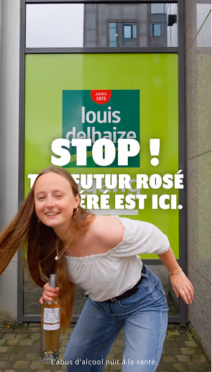blue2purple - A smiling woman holding a bottle of rose wine in front of a green Louis Delhaize advert