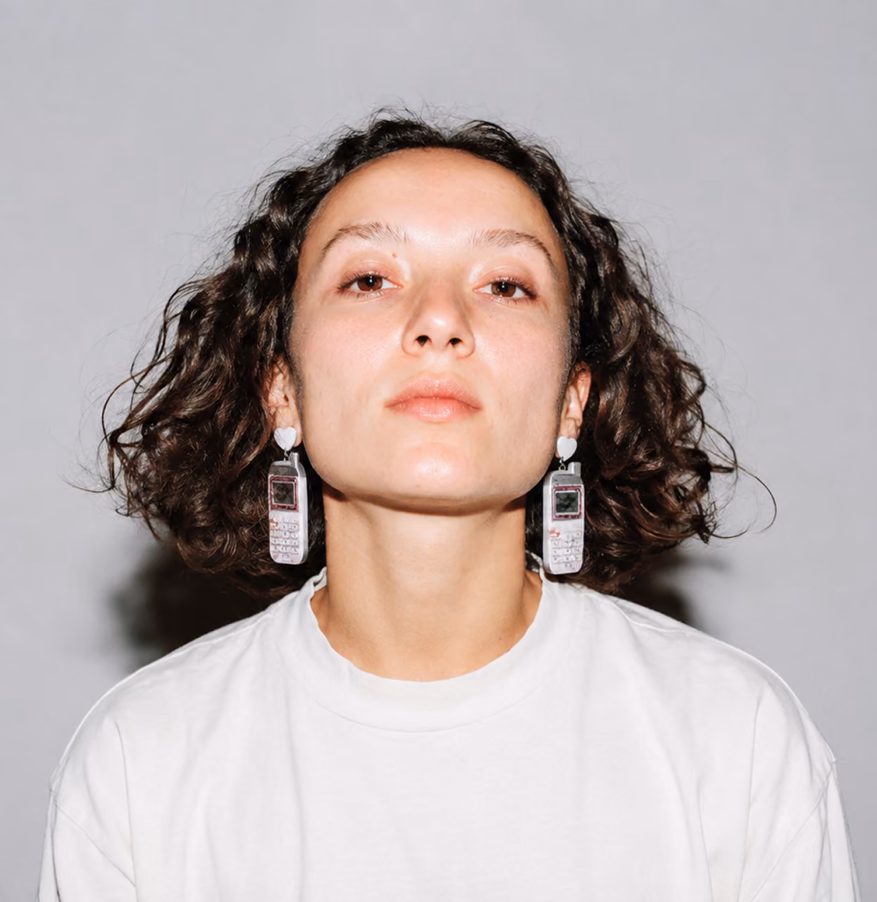 blue2purple - Studio portrait of a woman in a white t-shirt wearing novelty mobile phone earrings