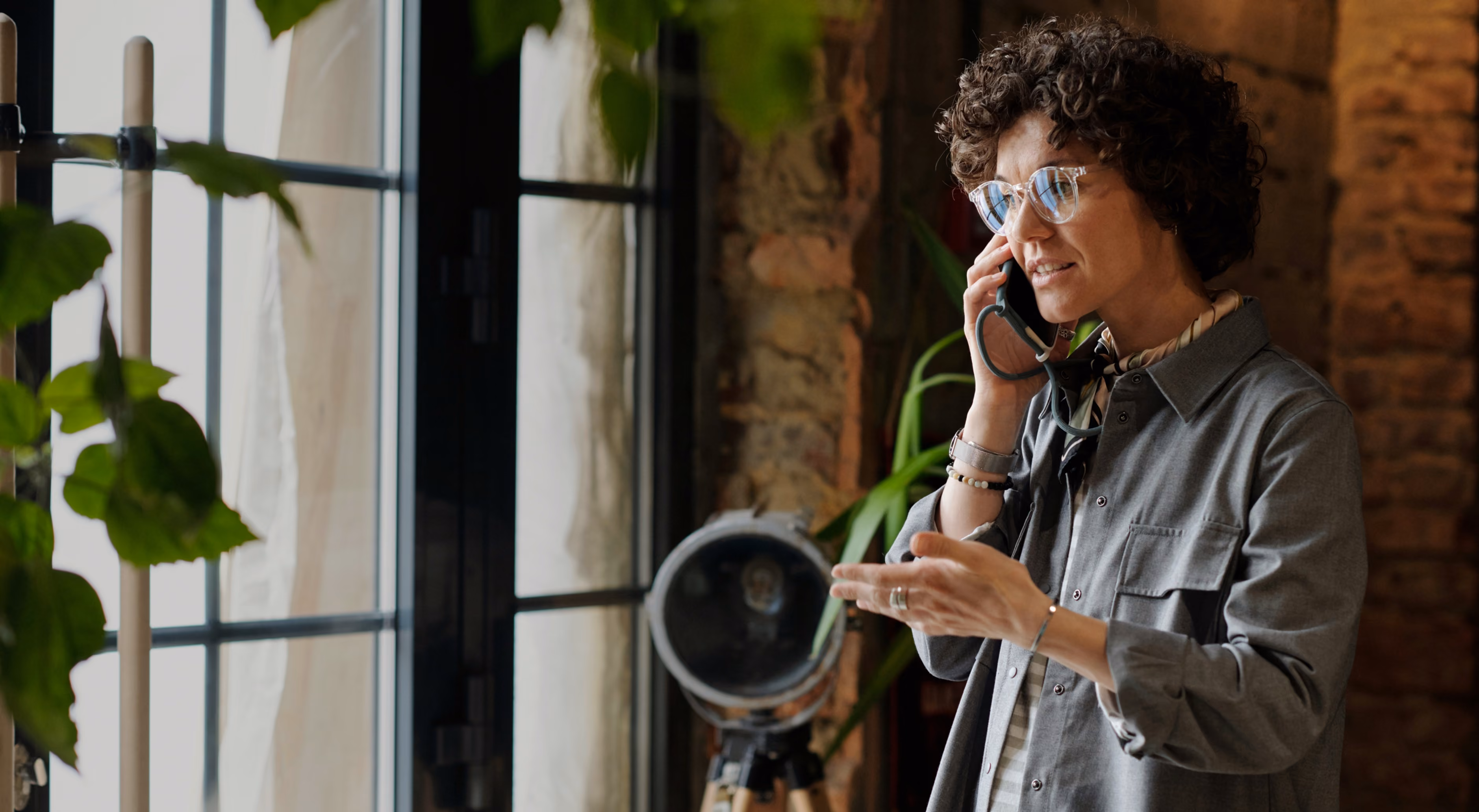 blue2purple - Woman with curly hair on the phone beside a window, holding a camera lens