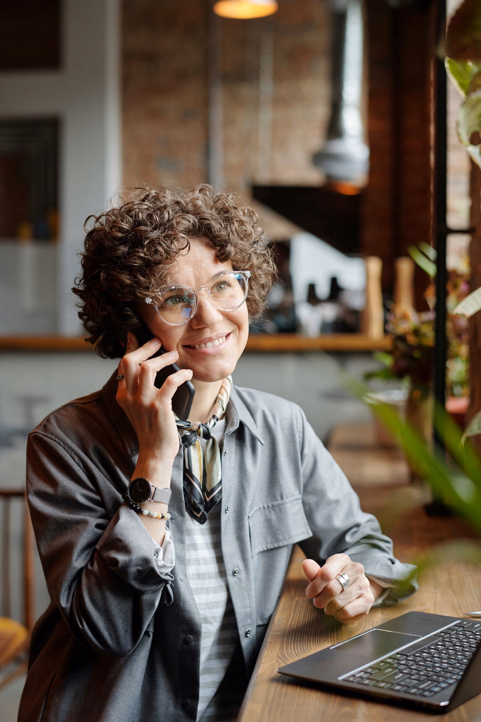 blue2purple - Smiling woman with curly hair on the phone at a desk with a laptop