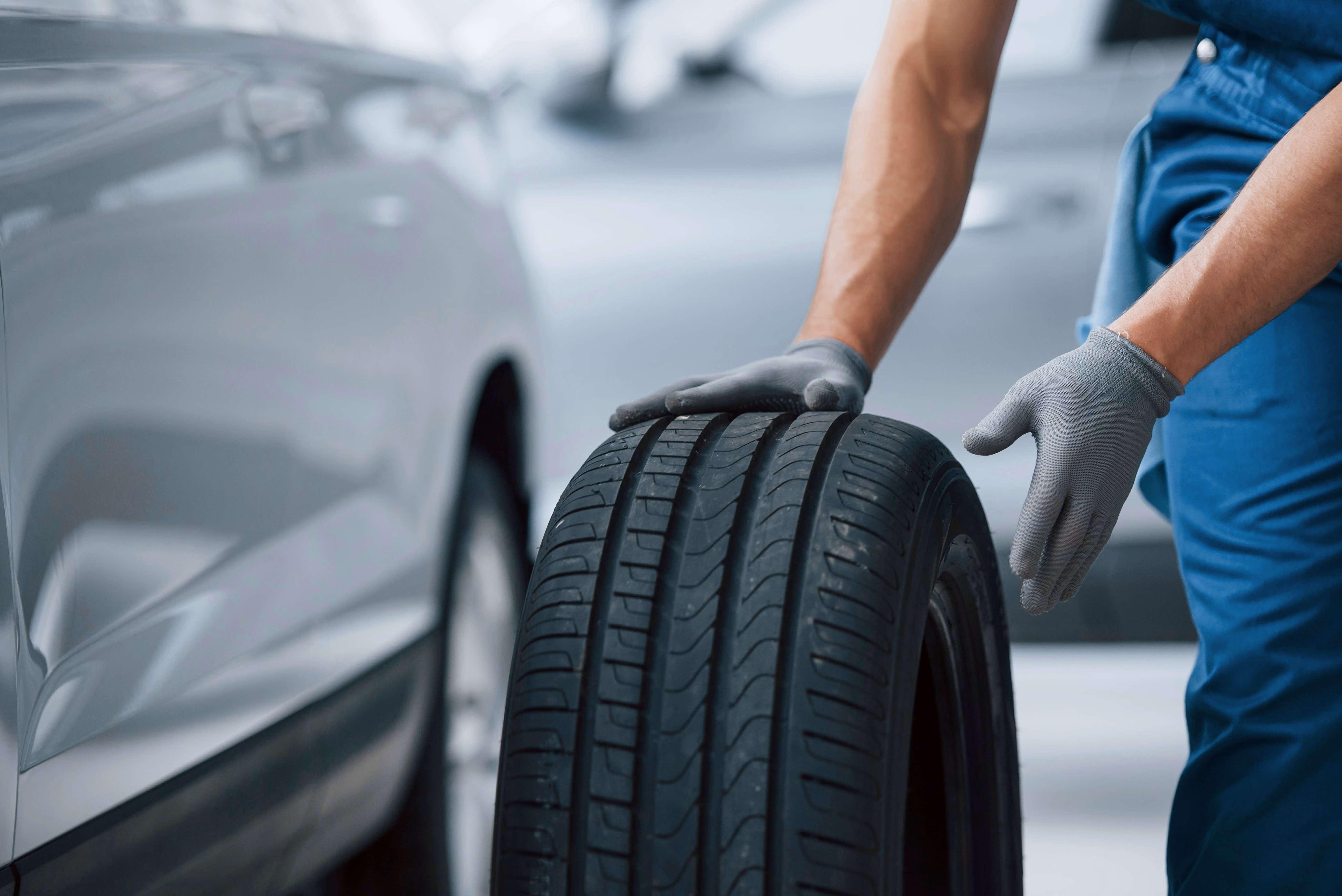 blue2purple - Mechanic in gloves carrying a tyre next to a car