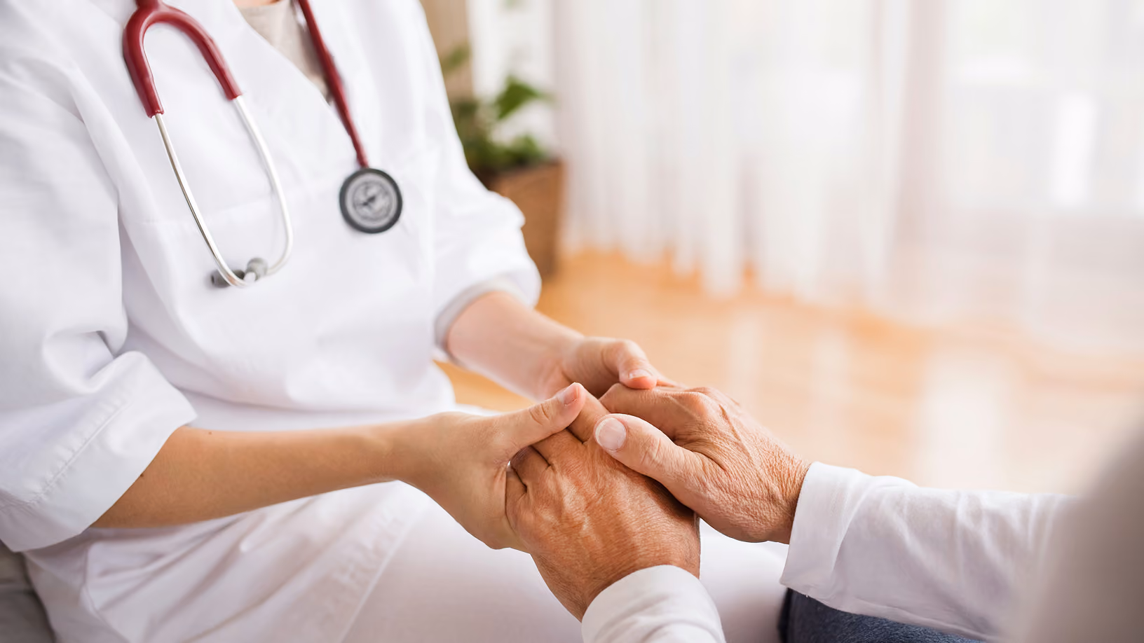 Healthcare provider gently holding an older patient's hands in a supportive gesture.