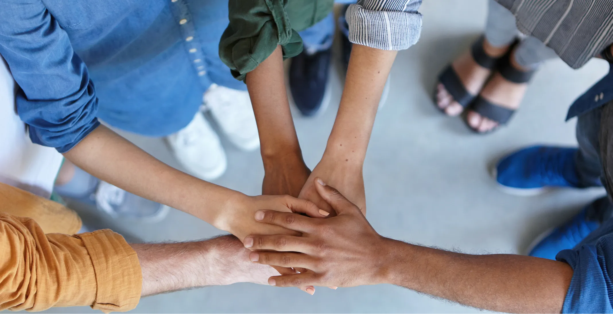Group of people placing their hands together in a team huddle, representing collaboration and teamwork.