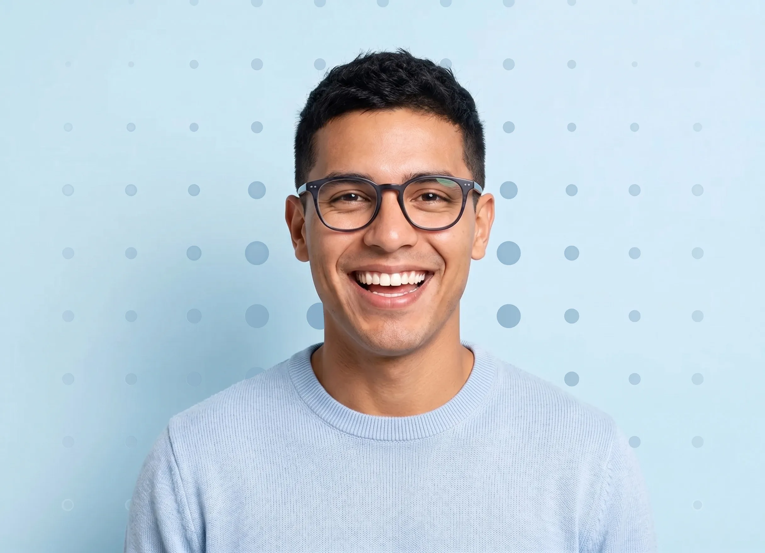 Smiling man with glasses wearing a light blue sweater against a blue background with dots.