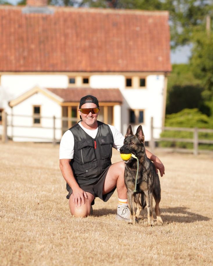 Scott McKay kneeling with German Shepherd Sonny on the paddock at Church Cottage