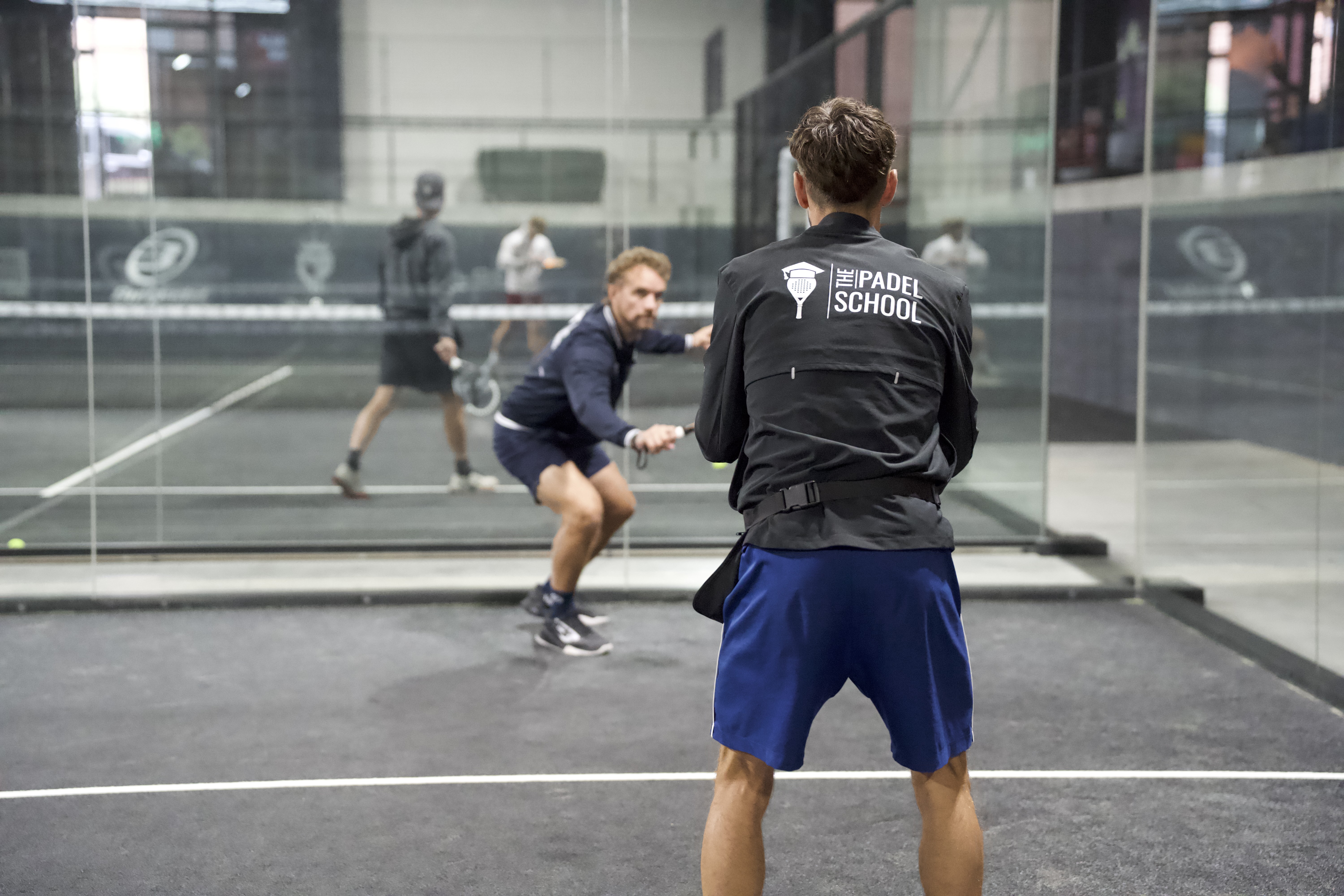 Padel coach watching a player practise a shot during an indoor lesson