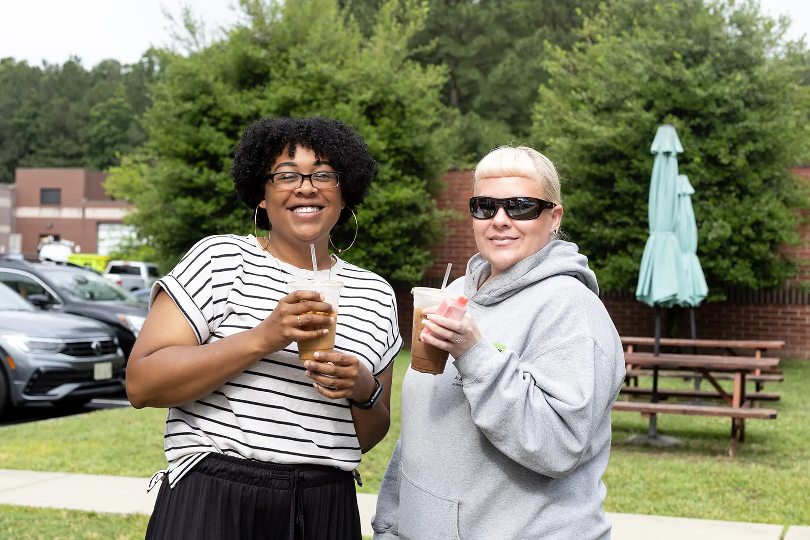 Two smiling guests holding iced coffees outside