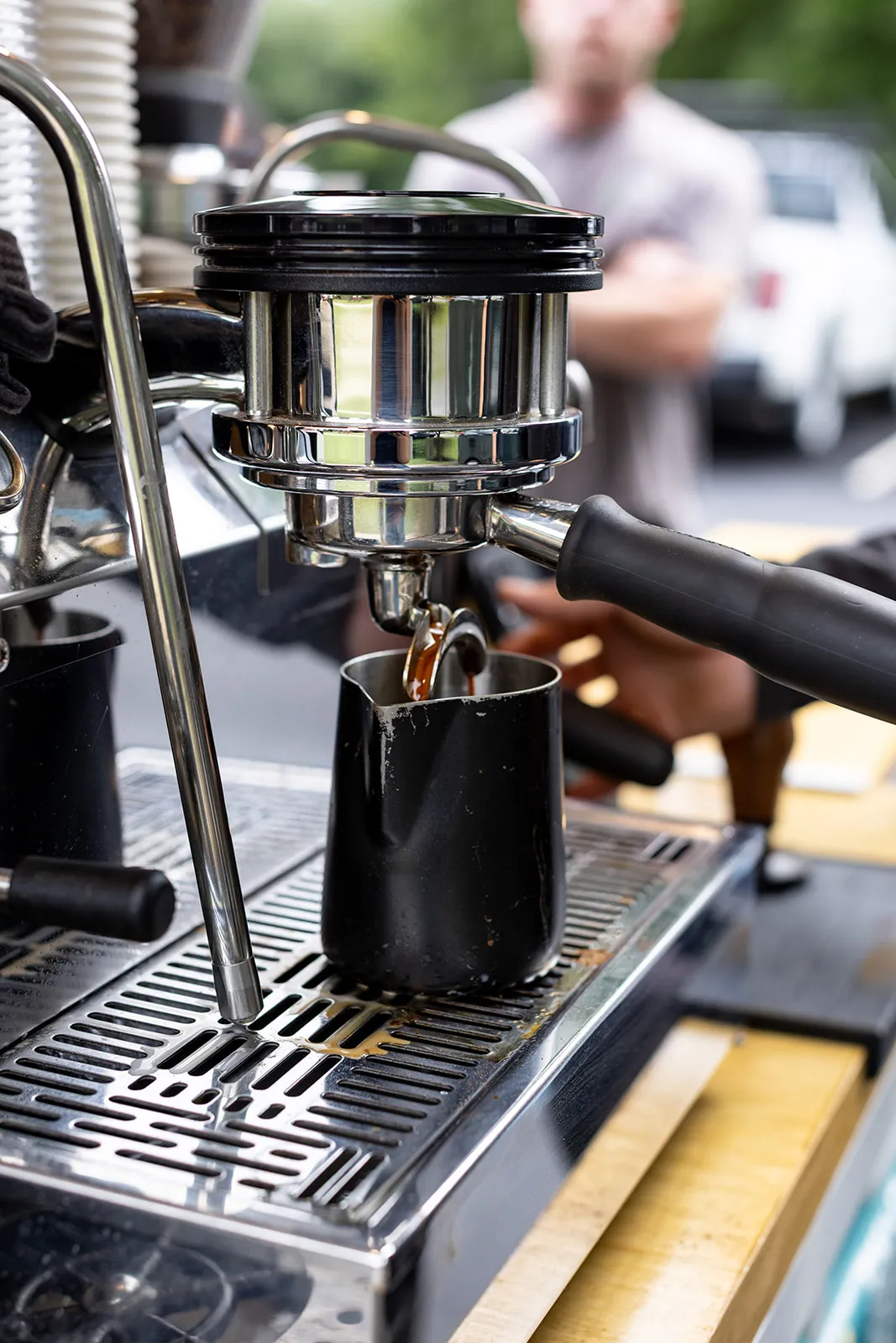 Espresso pouring from a portafilter into a black pitcher at an outdoor event